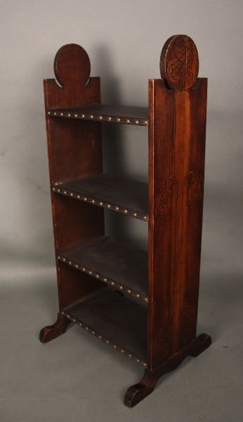An antique 11966. Arts And Crafts bookcase with etched sides and leather lined shelves, set against a gray background.