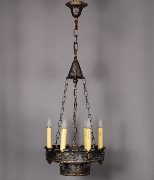 10008. 1920's Iron Chandelier With Cut Outs with weathered metal finish, suspended by chains, featuring four candle-shaped bulbs.