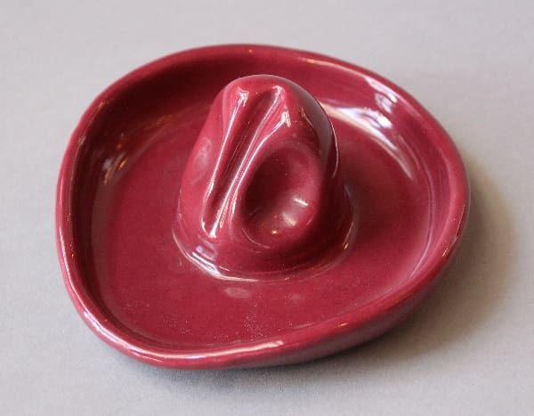 A red ceramic 10218. Monterey Period Sombrero Ashtray designed like a hand with a raised index and middle finger, positioned on a gray background.