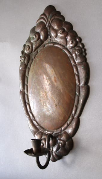 Antique oval wall mirror with a decorative floral frame and a 10220. Early 20th Century Copper Repousee Candle Sconce, mounted on a gray wall.