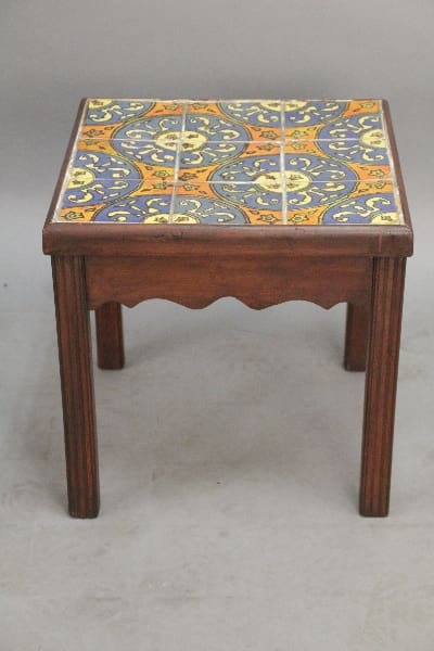 A small wooden stool with a colorful ceramic tile top featuring a blue and yellow ornate pattern, like the 10358. 1920's California Tile Table With 9 Tiles.
