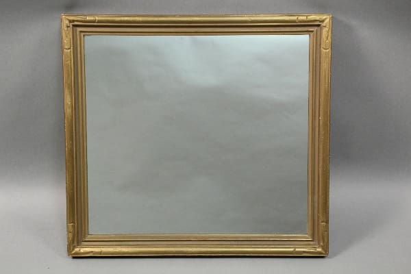 An ornate 10622. Large Scale 1920's mirror against a plain gray backdrop, reflecting a hazy, obscured image.