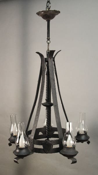 A vintage 11393. 1930's Monterey Period Chandelier With Glass Hurricanes with six arms, each holding a small glass hurricane lamp, hanging from a chain.