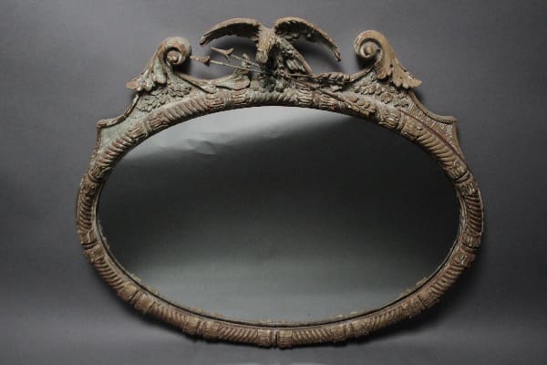 Antique oval mirror with ornate floral and bird design on the frame, set against a plain dark background. 12003. American Federal Carved Wood Mirror With Eagle