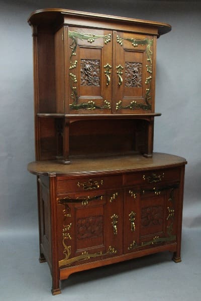 An antique 12593. Turn Of the Century Art Nouveau Cupboard with ornate carvings and brass hardware on a gray background.