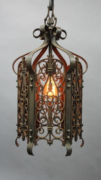 12595. Spanish Revival 1920's Pendant with intricate patterns, suspended from a chain, illuminated by a single glowing light bulb inside.