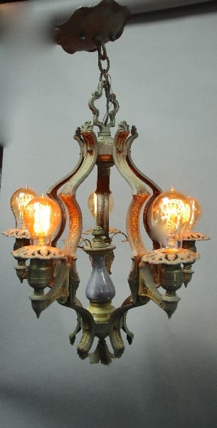 Vintage 12608. Spanish Revival 1920's Polychrome Chandelier With Steuben Center with three illuminated bulbs, reflected on a glossy surface below.