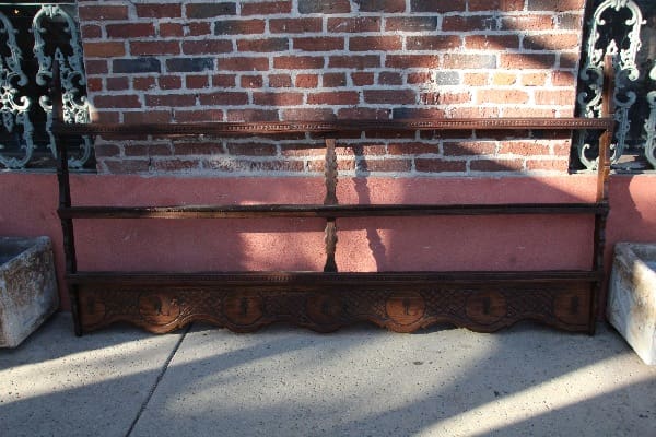 12902. Large 19th Century European Plate Rack with intricate carvings, positioned against a brick wall on a sunlit pavement.