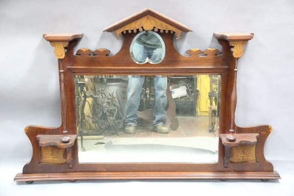 Antique 12989. Turn Of The Century Mirror with inlay and original bevel mirror mantel clock with a reflective glass front that shows a reflection of someone's legs and cluttered background.