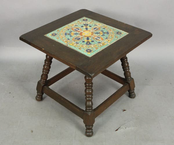 A small 13351. Spanish Revival Tile Table with decorative ceramic tile inset on top, featuring a colorful floral pattern, on a plain gray background.
