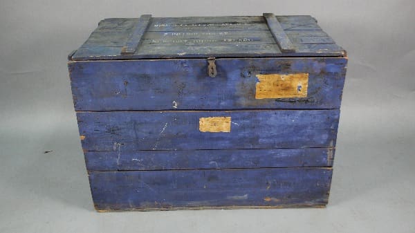Vintage blue wooden trunk with metal reinforcements and labels, placed against a grey backdrop.
