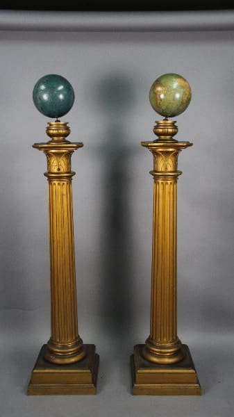 Two 13438. Pair Of Gilded Column With Globes, each topped with a globe, standing against a grey backdrop with a subtle shadow in the center.