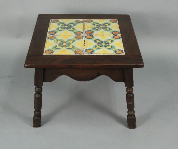 Spanish Revival D&M 1920's Tile Table with a decorative ceramic tile inlay on top, featuring a floral pattern. the table has ornate legs and a rich, dark finish.