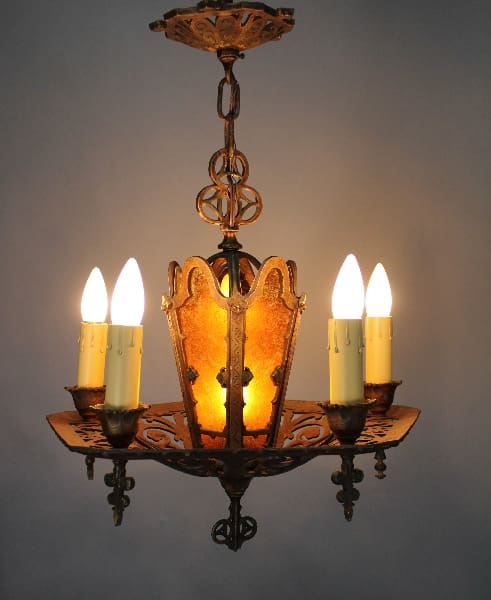13939. 1920's Polychrome Chandelier with ornate metal details and four lit electric candles, set against a warm glowing mica shade background.