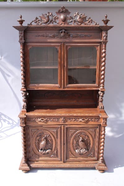 Antique wooden court cabinet with ornate carvings and glass doors, featuring spiral columns and relief panels with bird motifs.