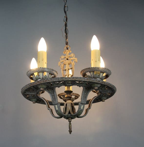 14001. Spanish Revival Five Light Chandelier Circa 1920's with three lit electric candles, ornate metal detailing, hanging from a chain against a gradient gray background.