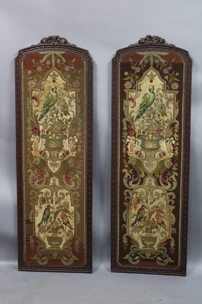 Two tall, ornate 14117. Pair of Turn Of the Century Framed Tapestries featuring colorful parrots perched on vases, surrounded by floral and scroll motifs, displayed against a gray backdrop.