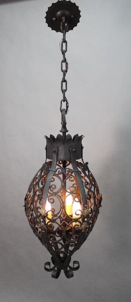 An 14261. 1920's Wrought Iron Pendant With Three Lights with intricate designs, suspended by a chain, emitting a soft glow from inside.