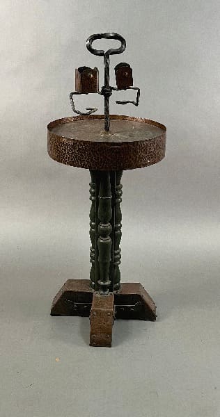 14355. Spanish Revival Copper And Wood Smoke Stand with a round, rusted seat and a chain-linked central support on an x-shaped base.