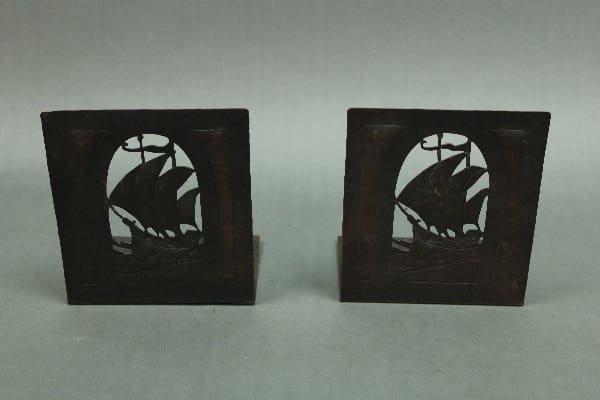 Two 14409. 1920's Spanish Revival Hammered Copper Book Holders depicting tall ships in sail, set against a grey background.