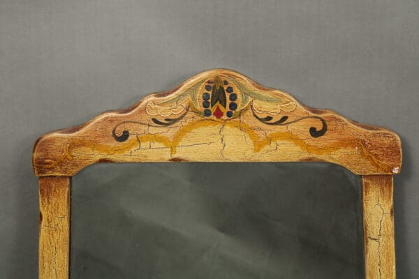 Close-up of a 14431. Hand Painted Mirror With Leather Detailing frame with decorative carvings and a colorful painted design on a gray background.