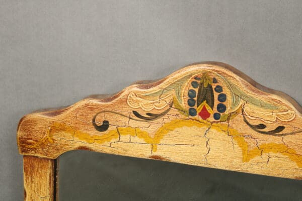 Close-up of a 14431. Hand Painted Mirror With Leather Detailing back with peacock feather motif carving and paint, showing signs of wear and aged texture.
