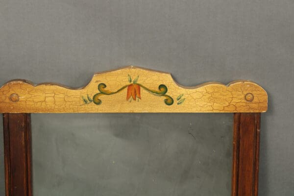 Top frame of a 14436. Monterey Period Spanish Revival Style Mirror featuring cracked paint, a central floral motif in red and green, and decorative wooden joints.