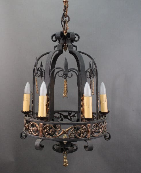 An ornate 14509. Outstanding Iron And Bronze Chandelier with four candle-shaped bulbs, detailed scrollwork, and a hanging chain, against a gray background.