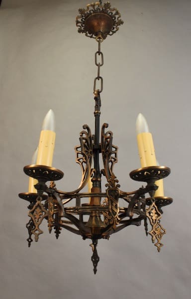 Sentence with Product Name: 14538. 1 of 2 Circa 1920's Bronze Chandelier With Shield Motif chandelier with intricate metalwork, featuring three electric candles and suspended from a ceiling mount.