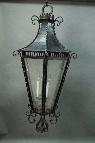 A vintage-style hanging lantern with metal frame and glass panels, featuring ornate details and containing two visible candle bulbs inside the 14599. Very Large 4 Ft High 1920's Original Iron Lantern.