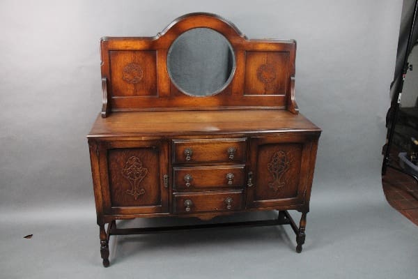 14814. Arts And Crafts Sideboard With Bird Motif with oval mirror and ornate carvings, featuring three drawers and two cabinets on a gray background.