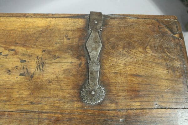 A close-up of a 14851. 19th Century Walnut Trunk With Original Hardware with a worn metal handle that has a decorative, floral end. the wood surface shows signs of aging and scratches.