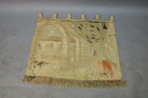 A worn-out rug with frayed edges and faded, abstract patterns displayed on a gray background.
