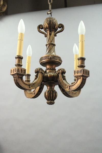 14895. Italianate Carved chandelier with five arms and candle-shaped bulbs, hanging from a ceiling, featuring ornate, metallic designs.