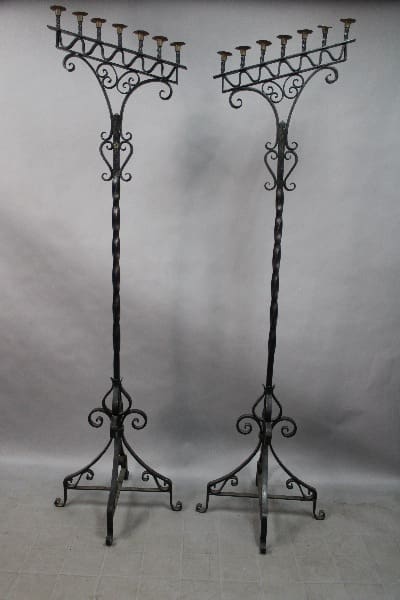 Two 14920. Rare Tall 1920's Pair Of Wrought Iron Torchieres with intricate designs, each holding multiple candles, against a gray backdrop.