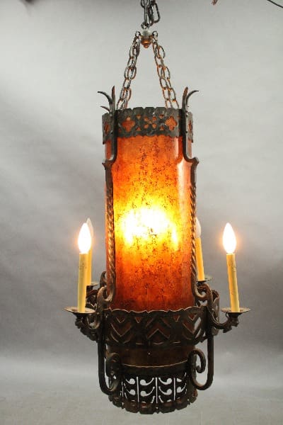 14921. 1 of 2 Spanish Revival 1920's Chandelier With Mica chandelier with orange glass panels and three lit candles, hanging against a grey backdrop.
