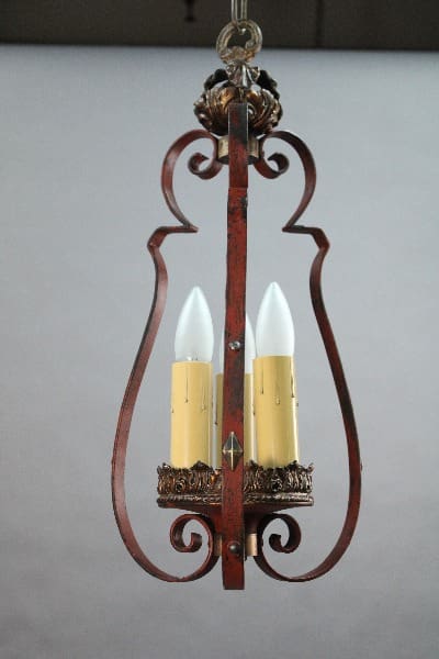 A vintage 15006 Spanish Revival pendant with three lights and a rusty iron frame and cream-colored faux candle covers.