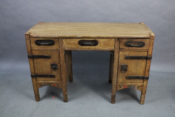 15010. Signed Monterey Desk With Original Iron Hardware with seven drawers, featuring metal handles and a weathered finish, positioned against a plain gray backdrop.
