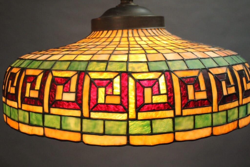 Close-up of an illuminated Turn Of The Century Art Glass Lamp Pendant With Greek Key motif featuring an intricate pattern of green, red, and yellow stained glass.