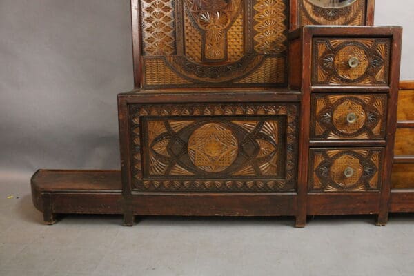 Antique wooden furniture featuring intricate carvings, including a chest, drawers, and a platform bed, displayed against a gray background.