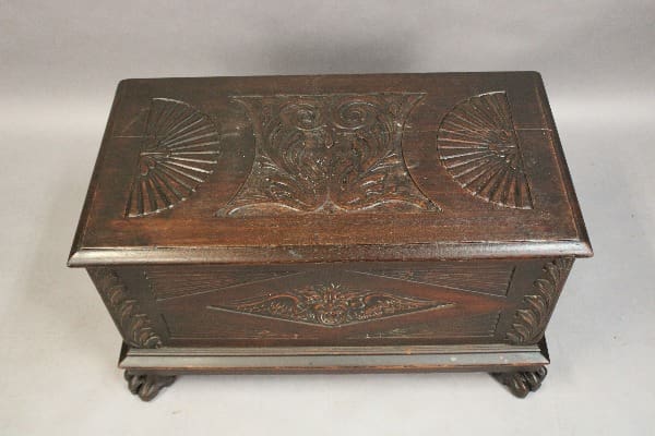 Sentence with the product name: 15154. 1920's Carved Trunk, featuring floral and fan motifs, resting on a simple platform.