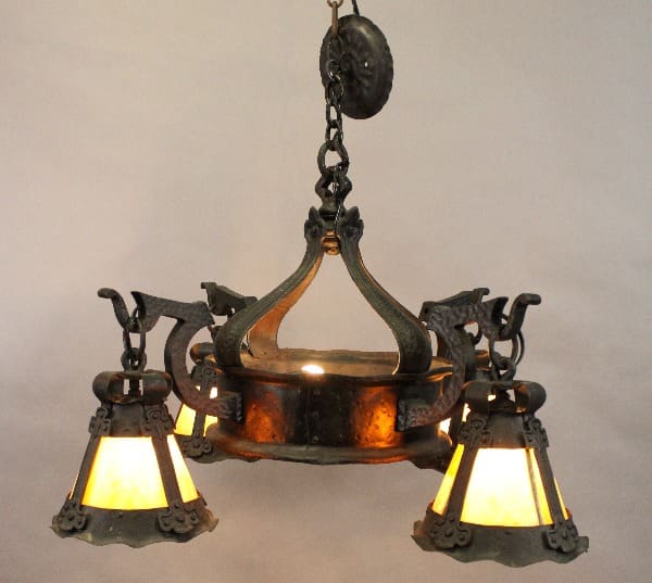 Turn of the Century chandelier with a central bowl and three ornate lamps featuring stained glass insets, illuminated against a gray background.