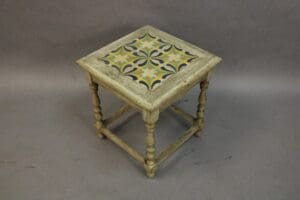 Antique wooden stool with decorative geometric ceramic tile inlay featuring ornate floral patterns, set against a plain gray background.