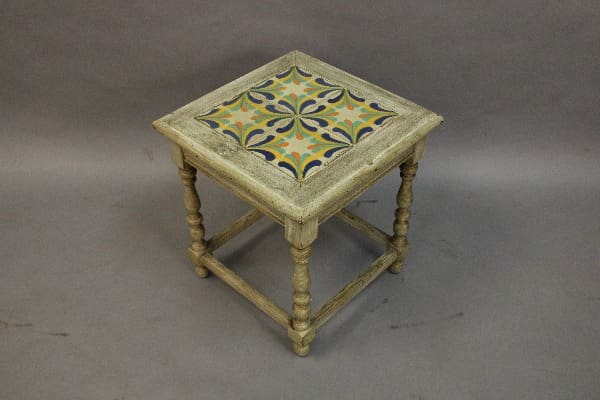 Antique wooden stool with decorative geometric ceramic tile inlay featuring ornate floral patterns, set against a plain gray background.