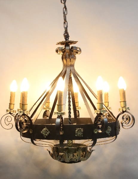 Sententence: 15342. Rare 1920's Large Scale Spanish Revival Chandelier with lit bulbs designed to resemble candles, adorned with metal scrolls and green crystal accents, set against a soft, warm background.