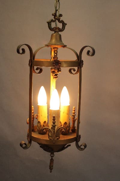 Vintage hanging lantern with 15389. 1920's Three Light Pendant With Original Polychrome Finish styled to look like candles, set against a plain background.