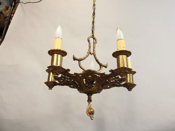 An antique brass chandelier with five arms, each holding a candle-shaped light bulb, and ornate decorations, suspended from a chain.