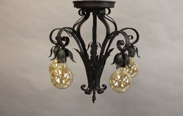Spanish Revival chandelier with ornate floral designs, featuring four illuminated, clear glass bulbs.