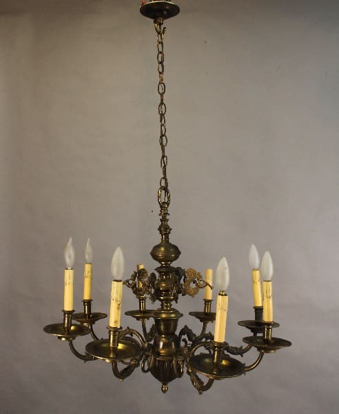 15511. 1920's Brass Chandelier With Nautical Mythical Figures with electric candles mounted on curved arms, hanging from a chain against a plain backdrop.