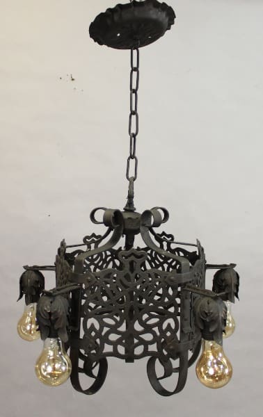 An antique 15591. Spanish Revival 1920's chandelier with intricate designs and four glowing bulbs, suspended from a decorative ceiling mount by a chain.